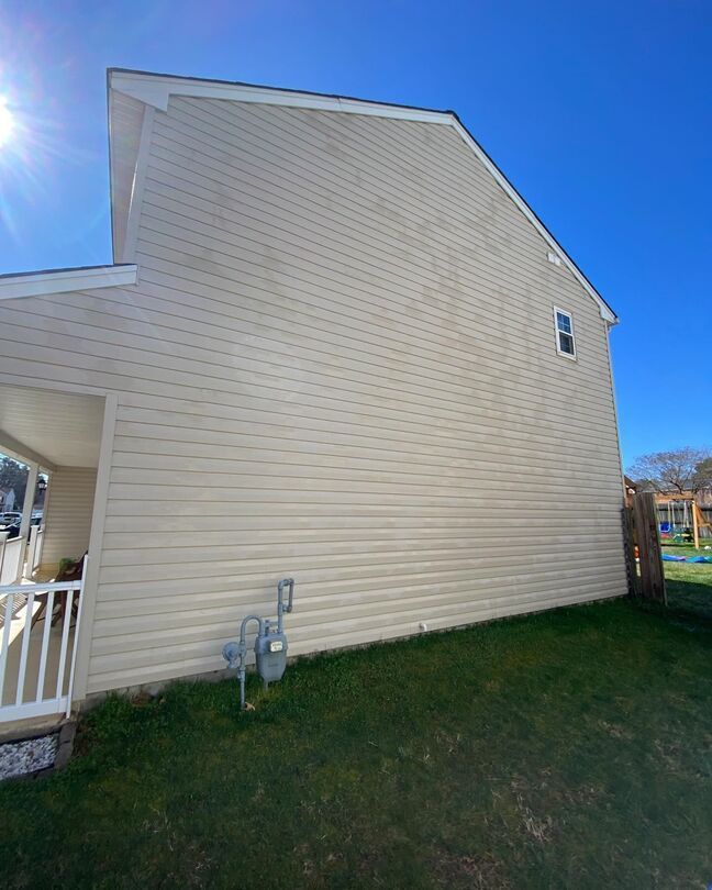 Beige house side wall with a small window, white porch railing, and green lawn under a blue sky