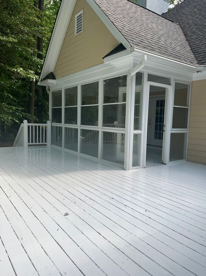 White screened porch and deck attached to a house, with trees in the background