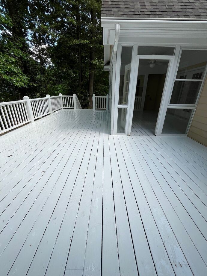 White wooden deck with railing beside a house and trees beyond