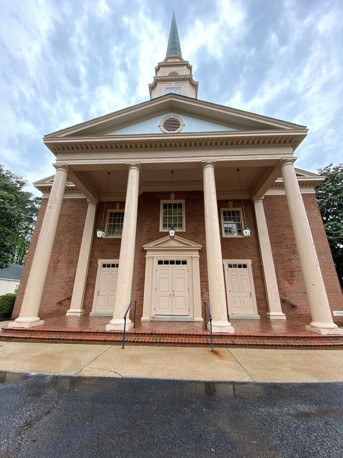 Brick church with white columns and steeple under a cloudy sky