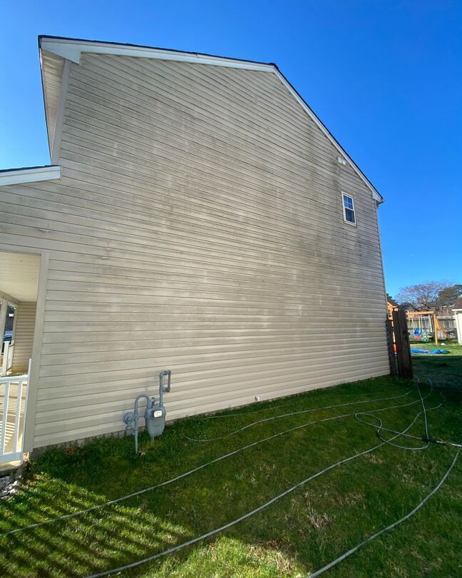 Beige house side wall with white siding, small windows, and a grassy yard under a clear blue sky