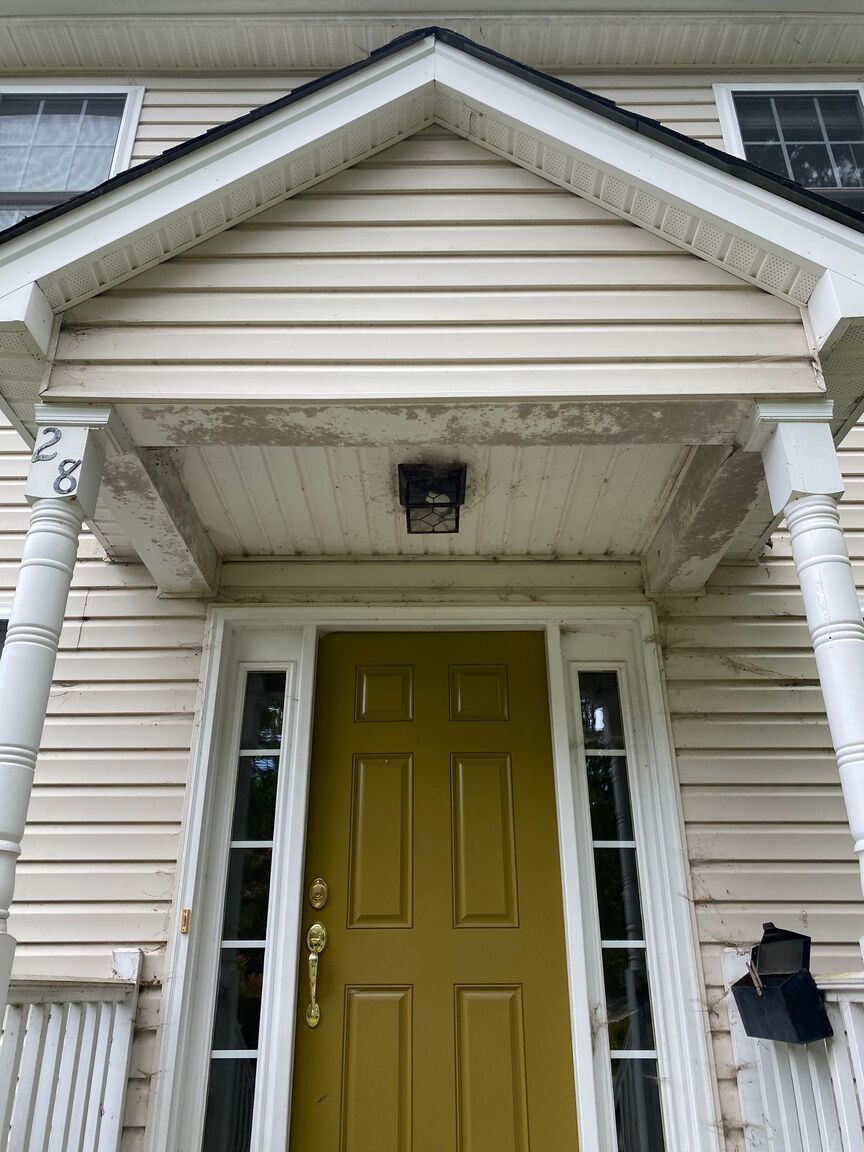Front entry with yellow door, white siding, and small porch roof above the doorway