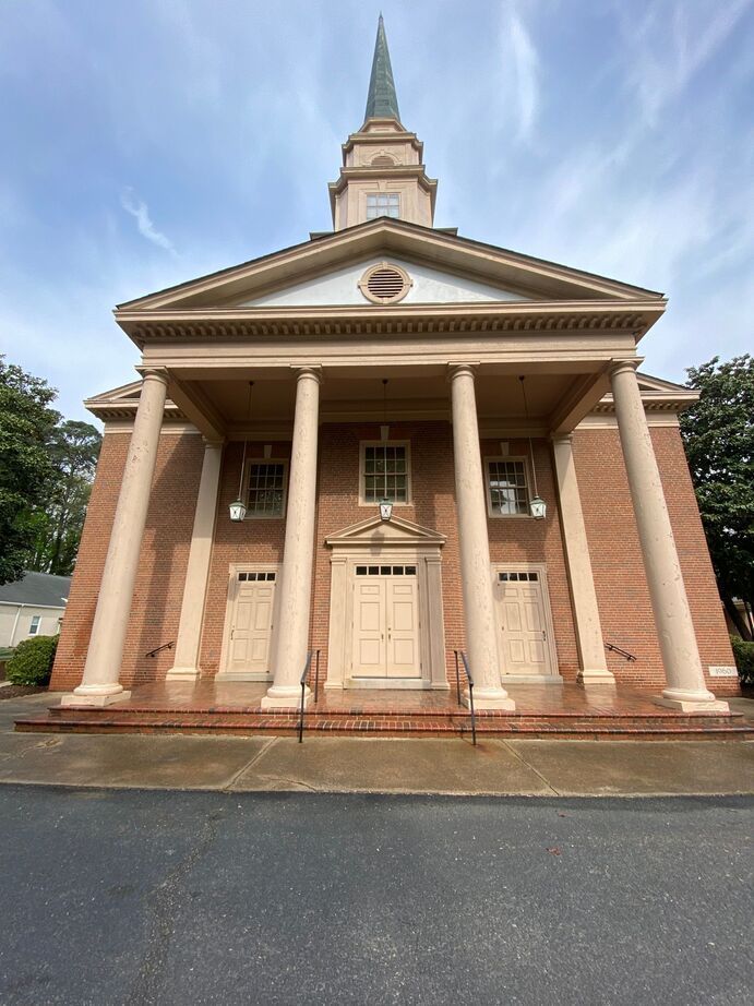 Front view of a brick church with white columns and a tall steeple under a cloudy sky