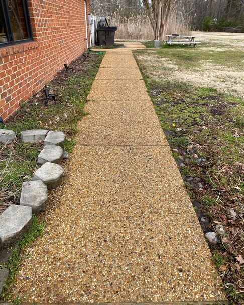 Gravel walkway beside a brick building, bordered by stones and leading through a yard.