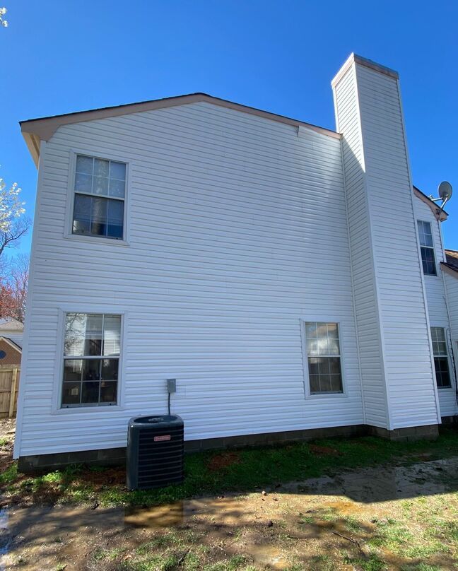 White two-story house with black-trimmed windows and a tall brick chimney on a sunny day.