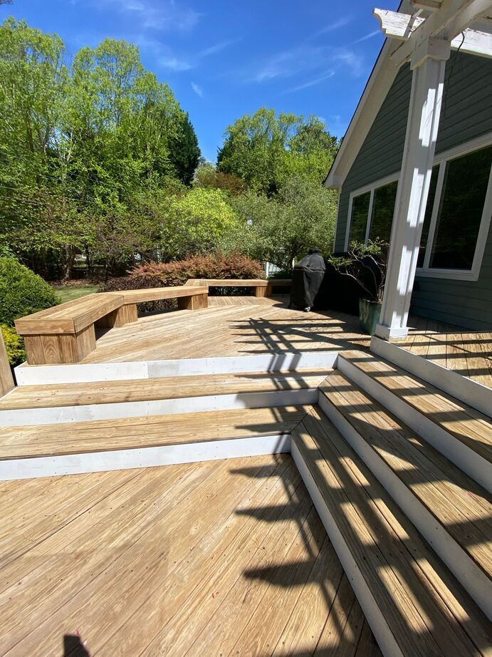 Backyard patio with wood deck steps, stone seating wall, and green trees under a blue sky