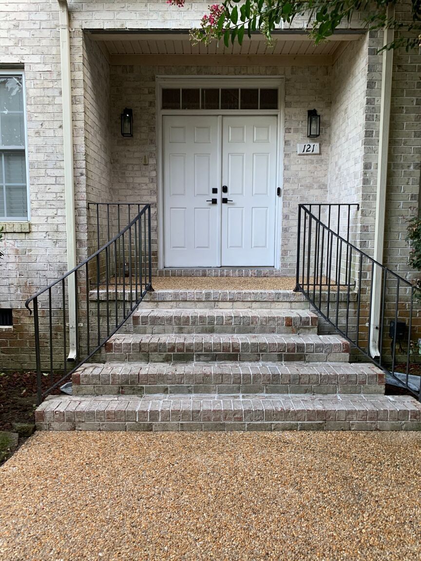 Front entry with white double doors, stone steps, black railings, and pebble walkway.