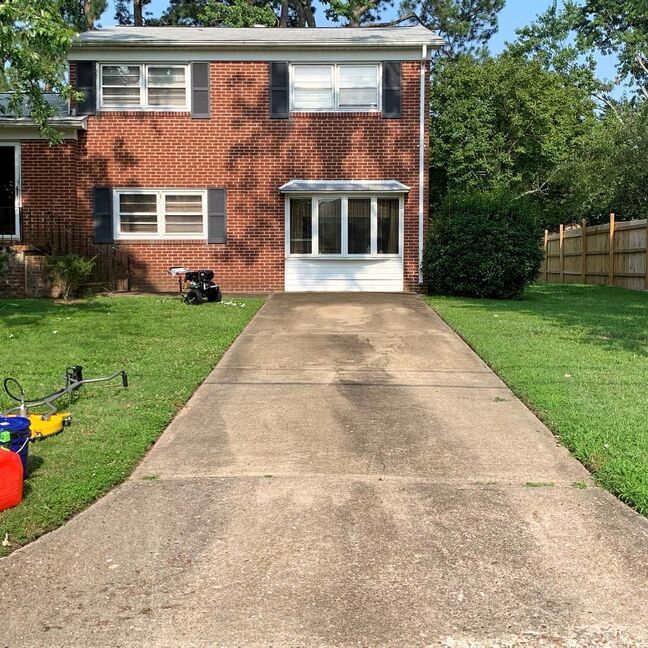Two-story brick house with a concrete driveway and green lawn on a sunny day