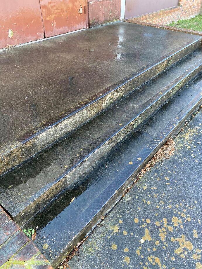 Wet concrete steps beside a rusty metal wall, with a shallow drainage channel and scattered leaves.
