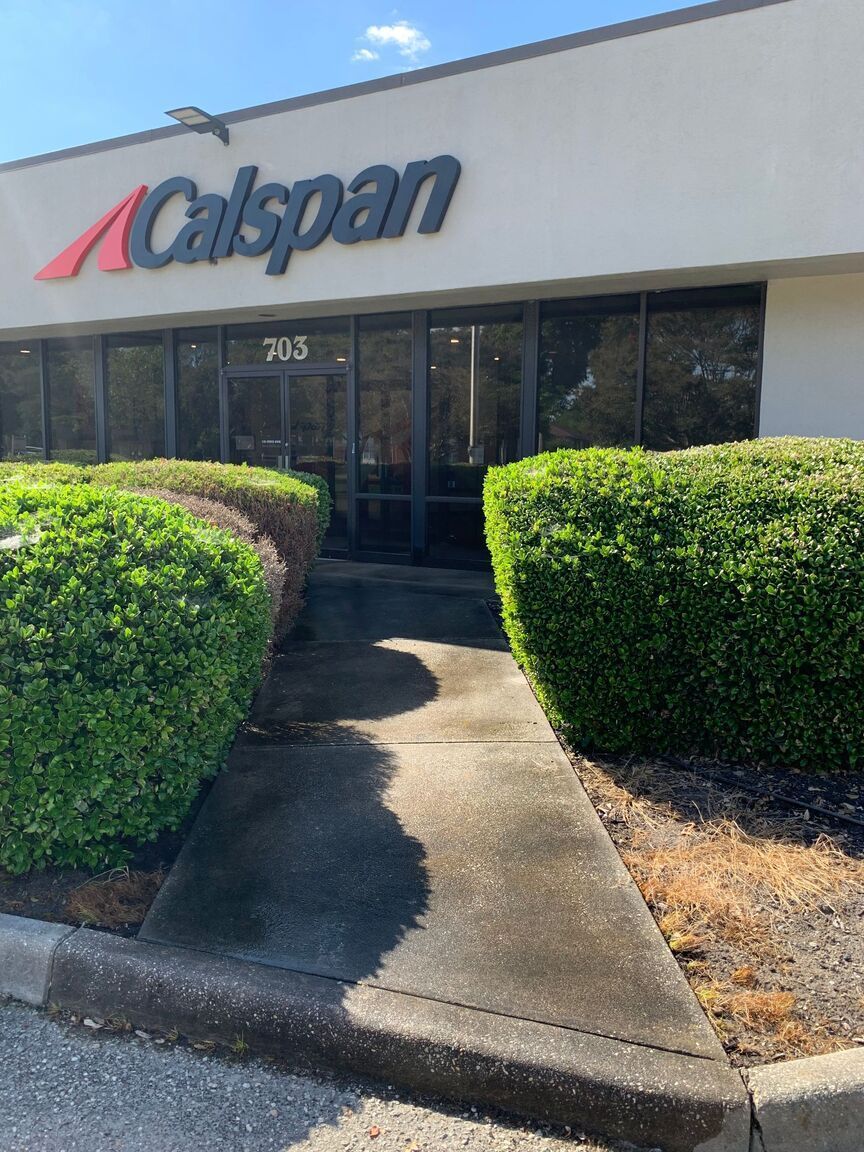 Calspan office entrance with glass doors, sign, and trimmed hedges along the walkway