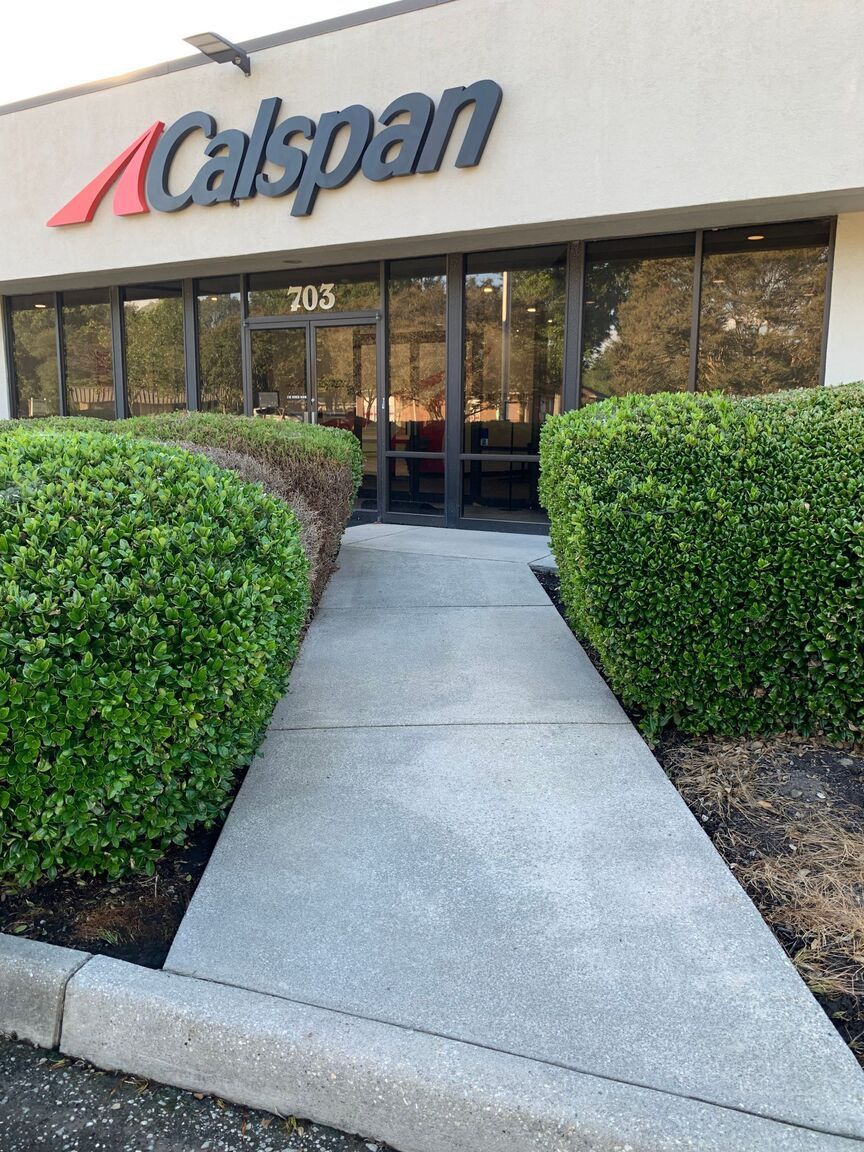 Calspan office entrance with trimmed hedges and a concrete walkway leading to glass doors