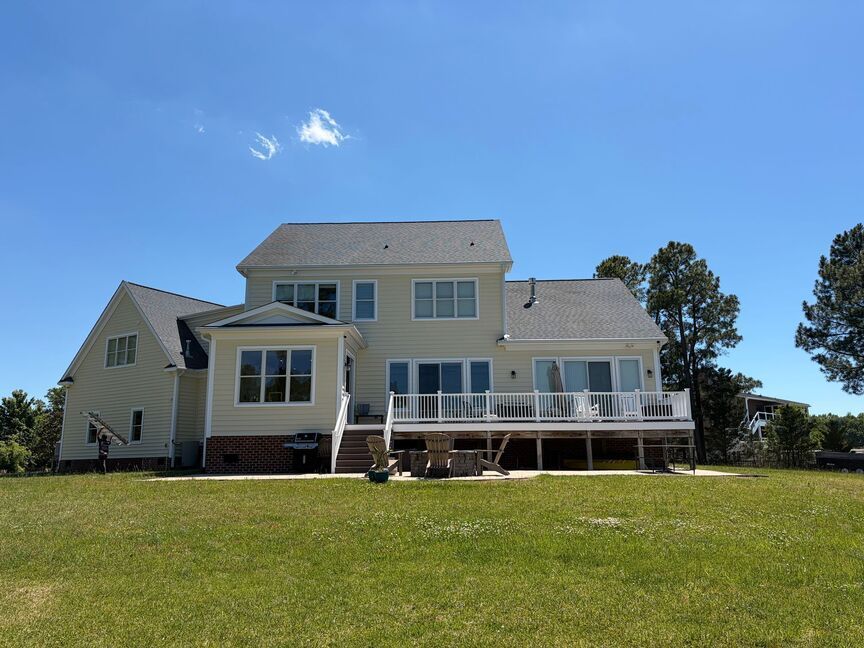 Large beige house with a deck on a grassy hill under a clear blue sky