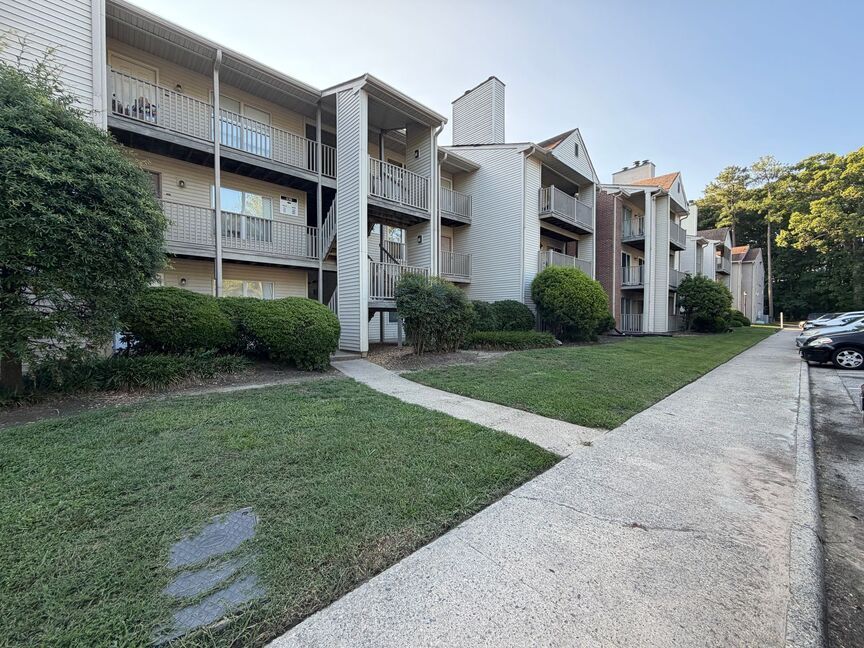 Apartment complex with white balconies, green lawn, and a paved sidewalk along the buildings
