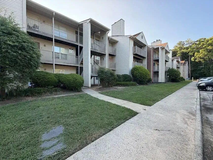 Apartment complex with white balconies, green lawn, and a paved sidewalk along the buildings