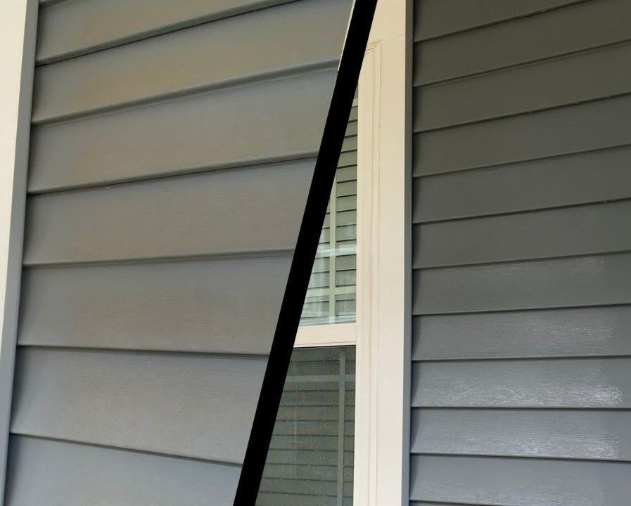 Close-up of gray house siding with a narrow vertical window between two angled wall sections