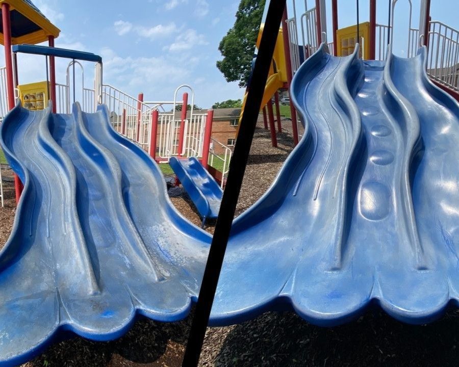 Blue wavy playground slides side by side with red railings under a sunny sky