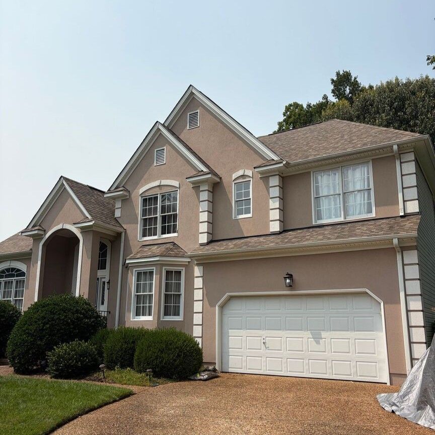 Suburban two-story beige house with a white garage, arched entryway, and manicured shrubs