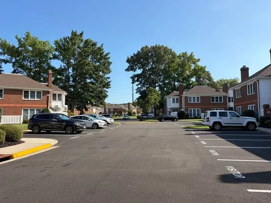 Apartment parking lot with parked cars, brick buildings, and trees on a sunny day