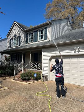 Person pressure washing a two-story house’s garage in a sunny yard.