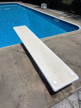 White diving board beside a blue swimming pool on a concrete deck