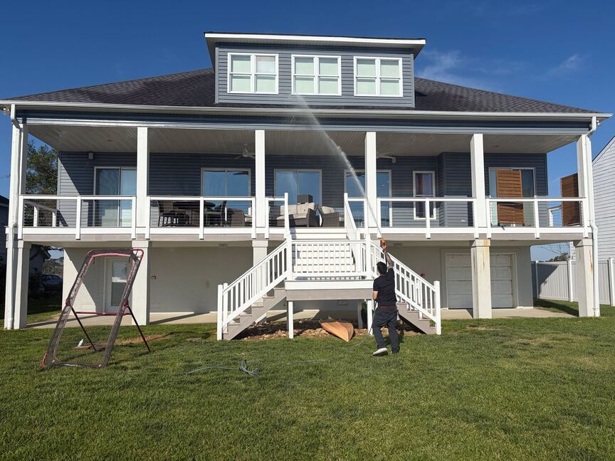 Two-story white house with a large porch, front stairs, and a person standing on the lawn