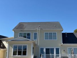 Two-story beige house with white trim and a ladder against the front under a clear blue sky