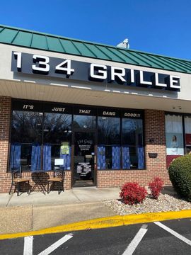 Storefront of 134 Grille restaurant with green roof, brick exterior, and patio seating outdoors
