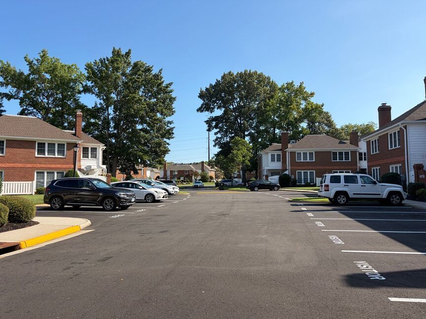Apartment parking lot with parked cars, brick buildings, and trees on a sunny day