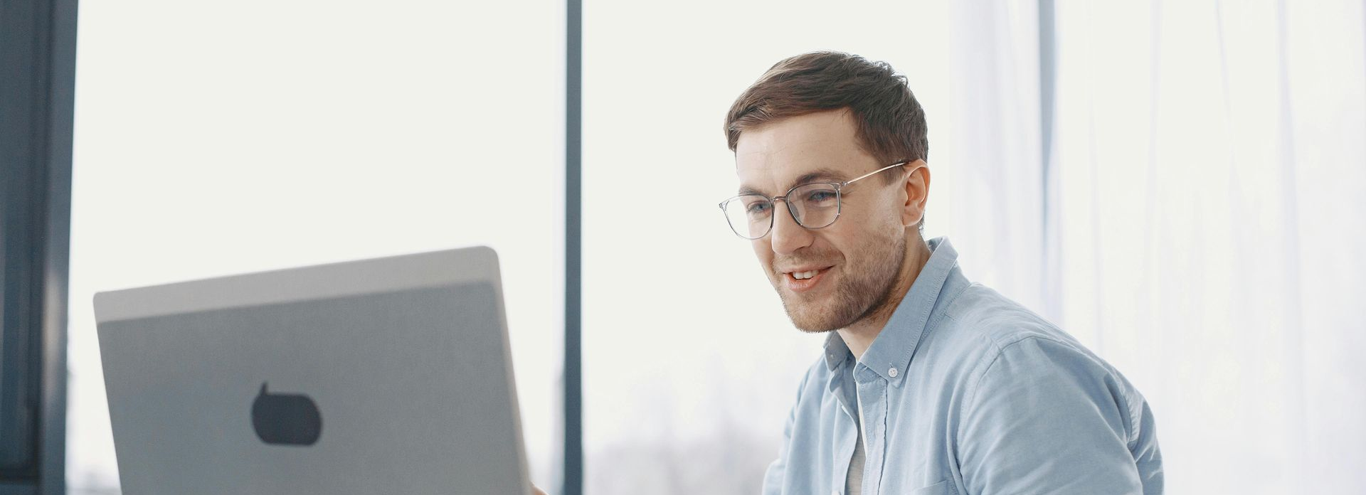 Smiling woman with glasses, lit by pink and teal lights, looking at a laptop.