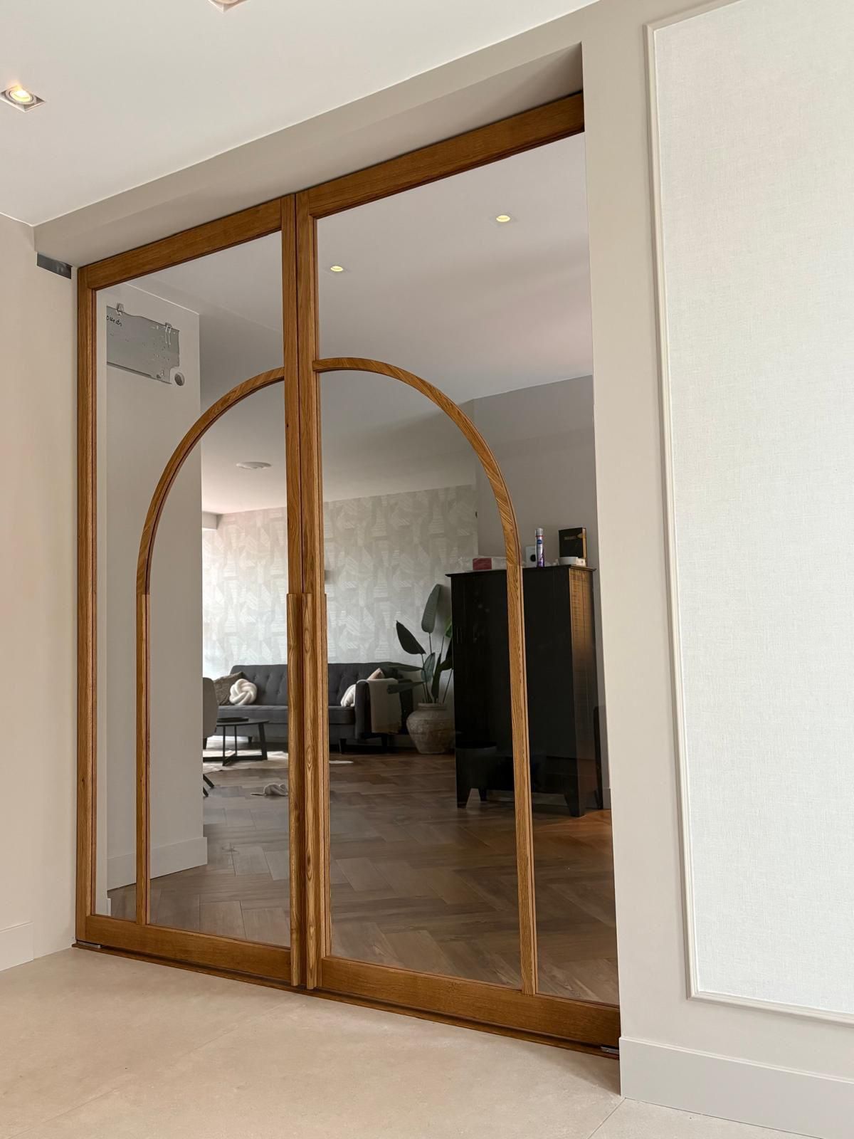 Dubbele eiken taatsdeur met helder gelaagd glas. Deuren vormen bij elkaar een organische boog en hebben een ronde greep.