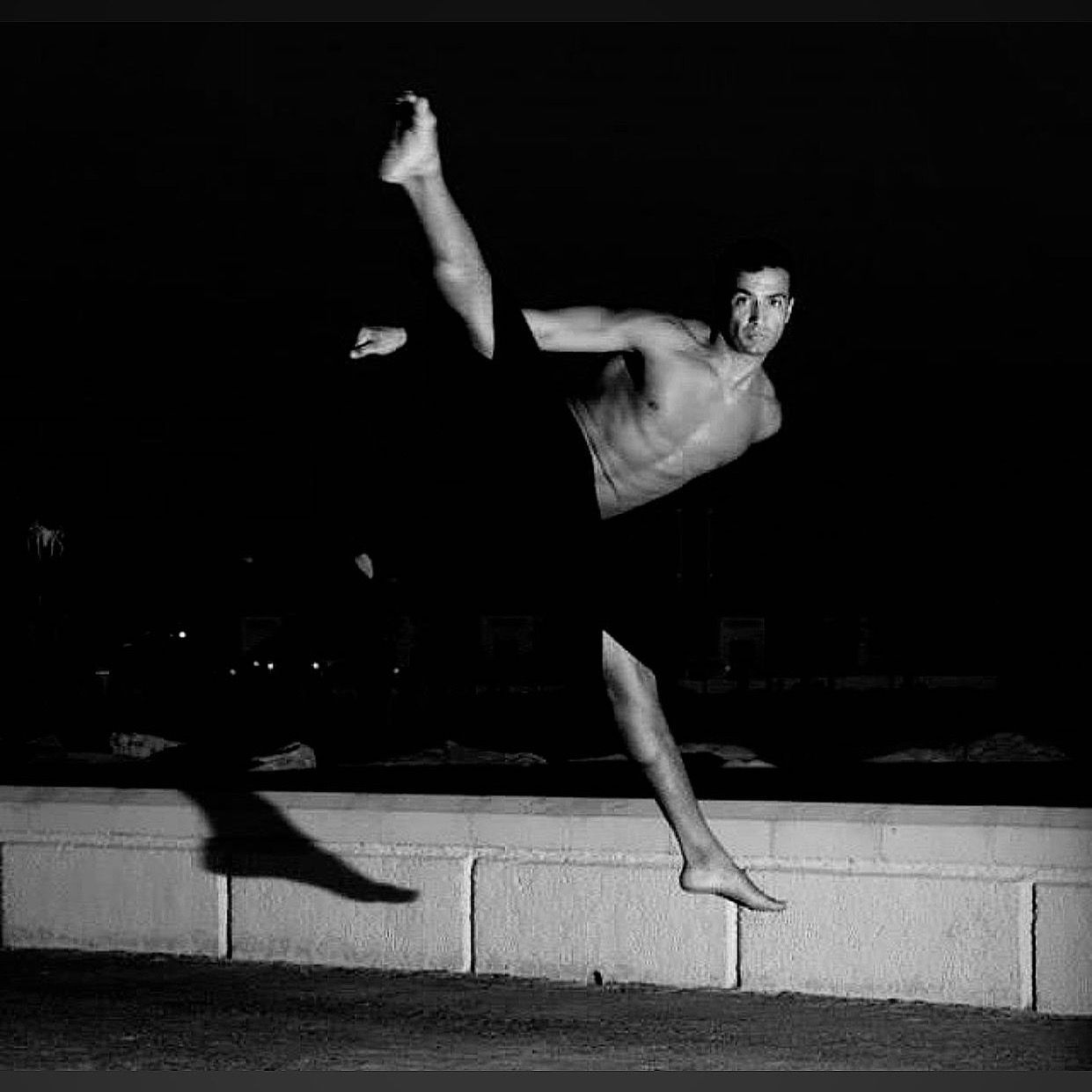 A man is doing a split on a wall at night.