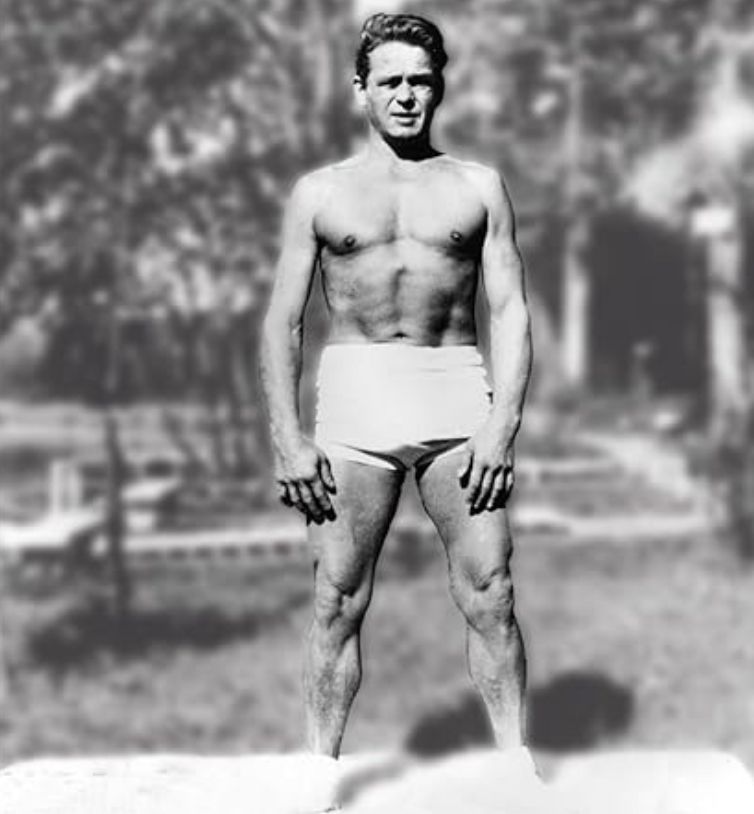 A shirtless man in white shorts is standing in a park.