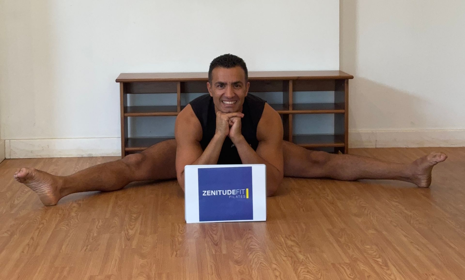 A man is doing a split on the floor with a box in front of him.
