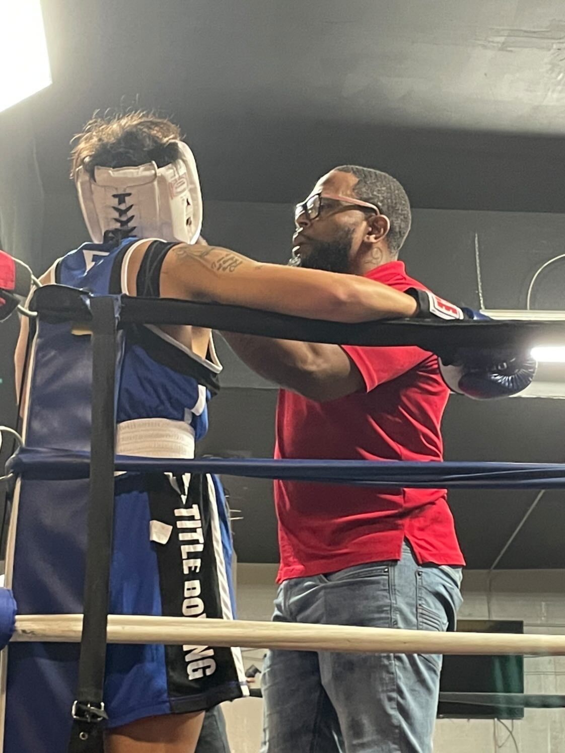 A man in a red shirt is helping another man in a boxing ring