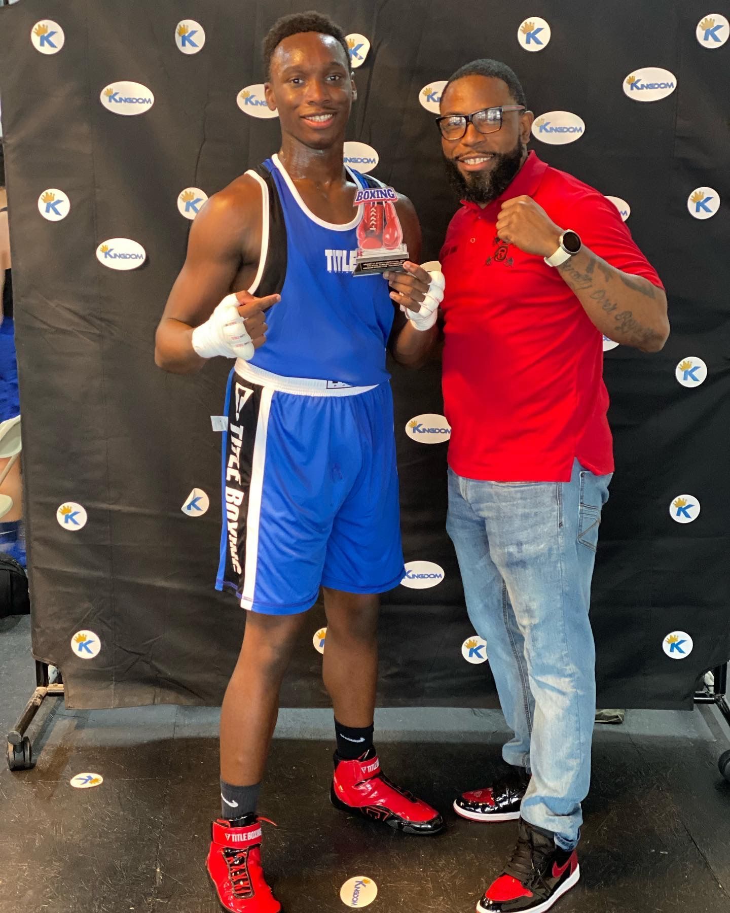 A man in a red shirt is standing next to a boxer holding a trophy.