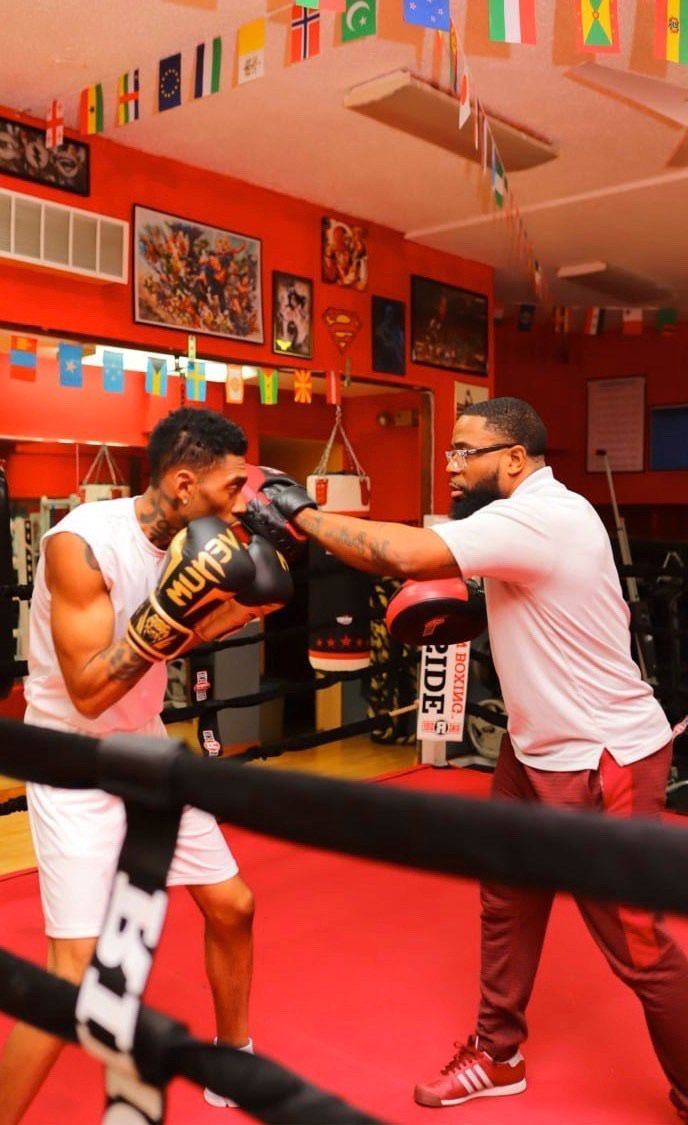 Two men are boxing in a gym with flags hanging from the ceiling.