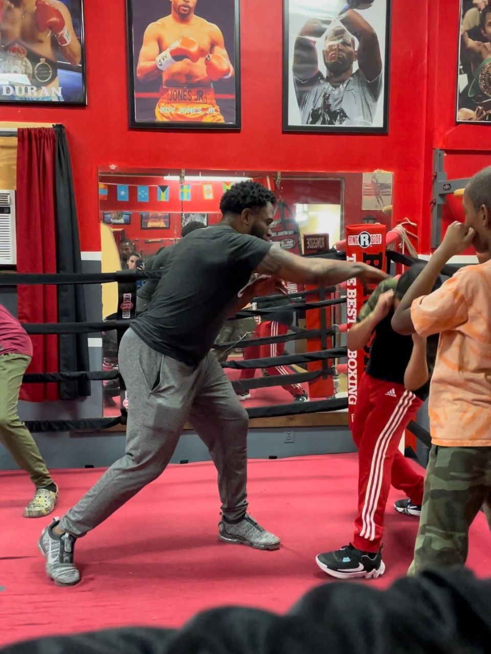 A man is teaching a group of children how to box in a boxing ring.