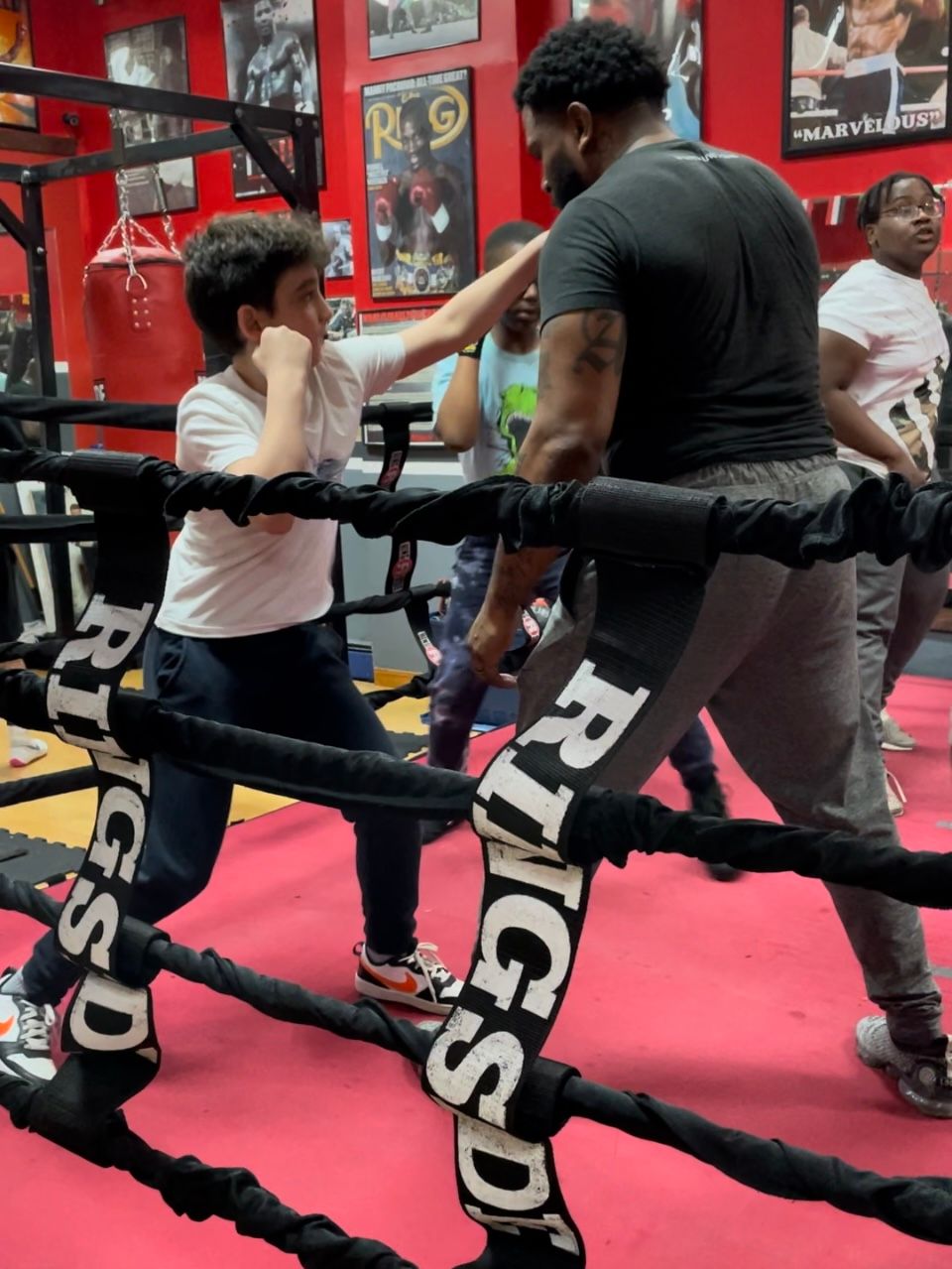 A man is teaching a young boy how to box in a ring that says rigsd on it