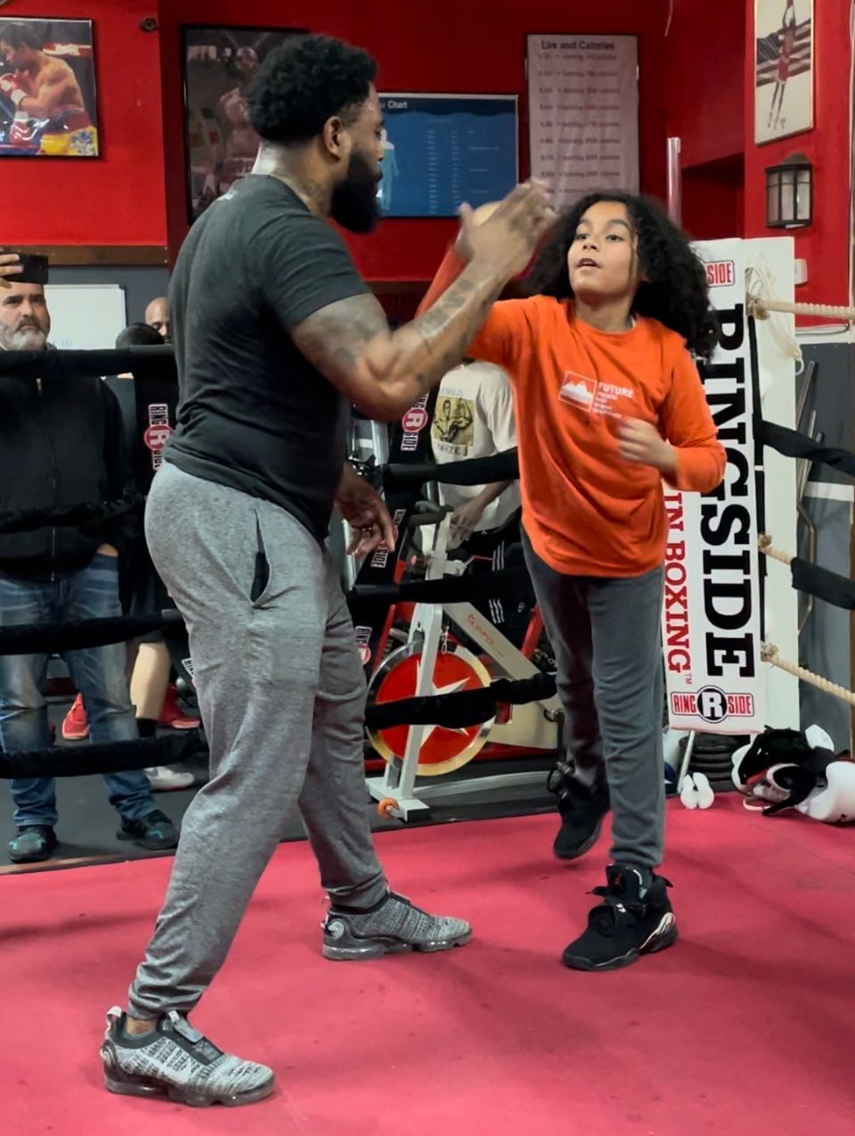 A man is teaching a little girl how to box in a ring that says ringside on it
