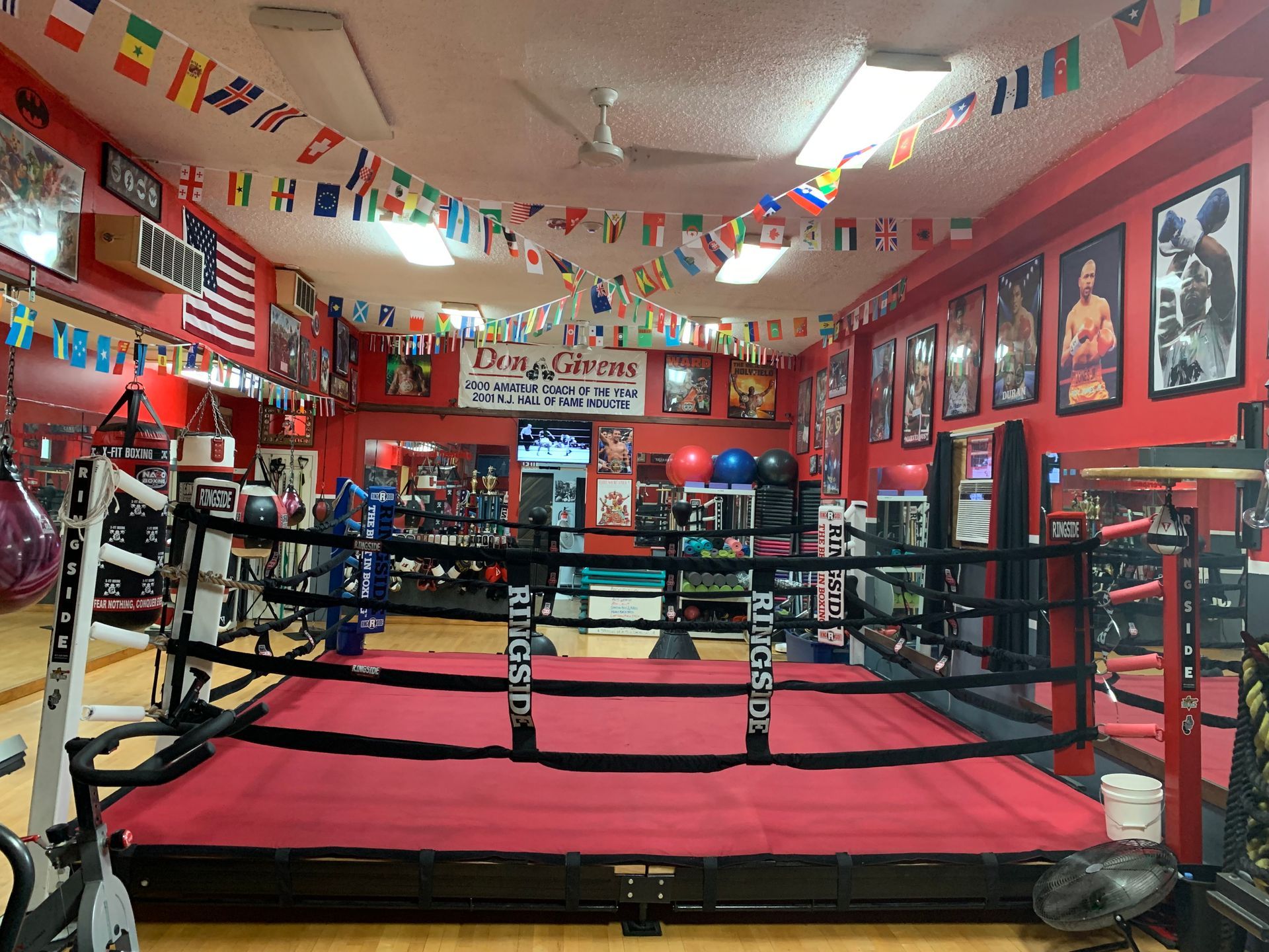 A boxing ring in a gym with flags hanging from the ceiling.