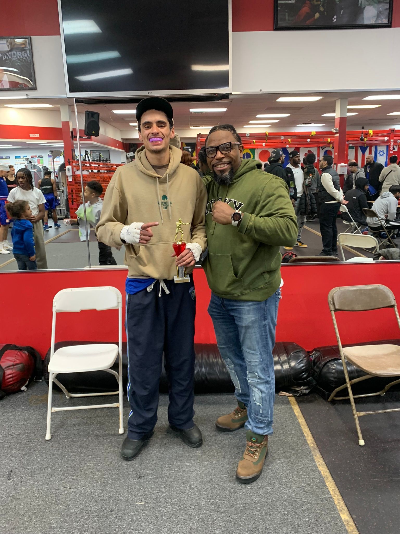 Two men are standing next to each other in a gym holding a trophy.