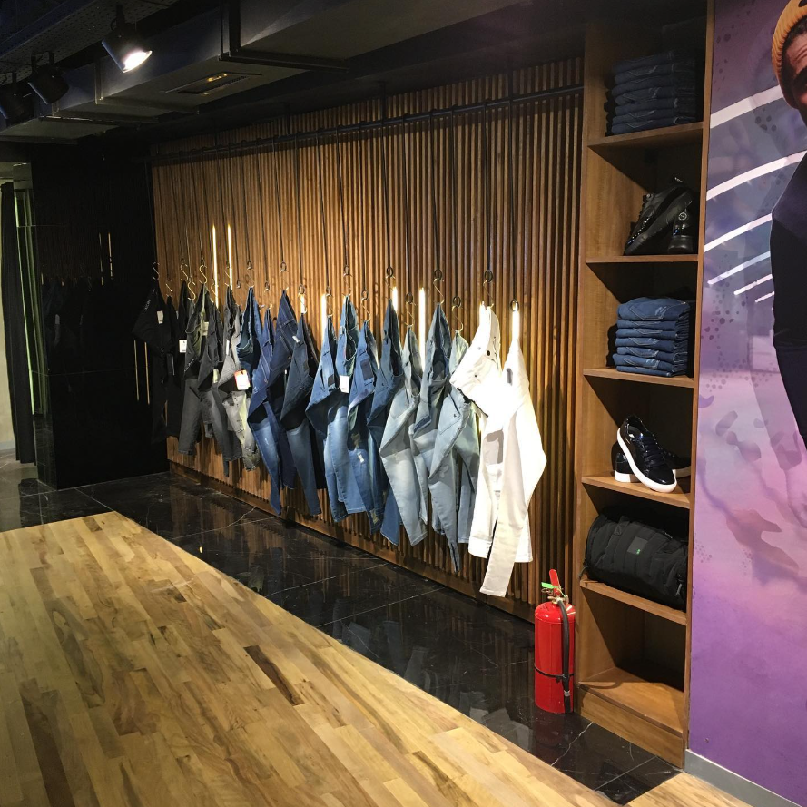 Interior de una tienda de ropa con jeans y camisas en exhibición, detalles de madera y un extintor de incendios.