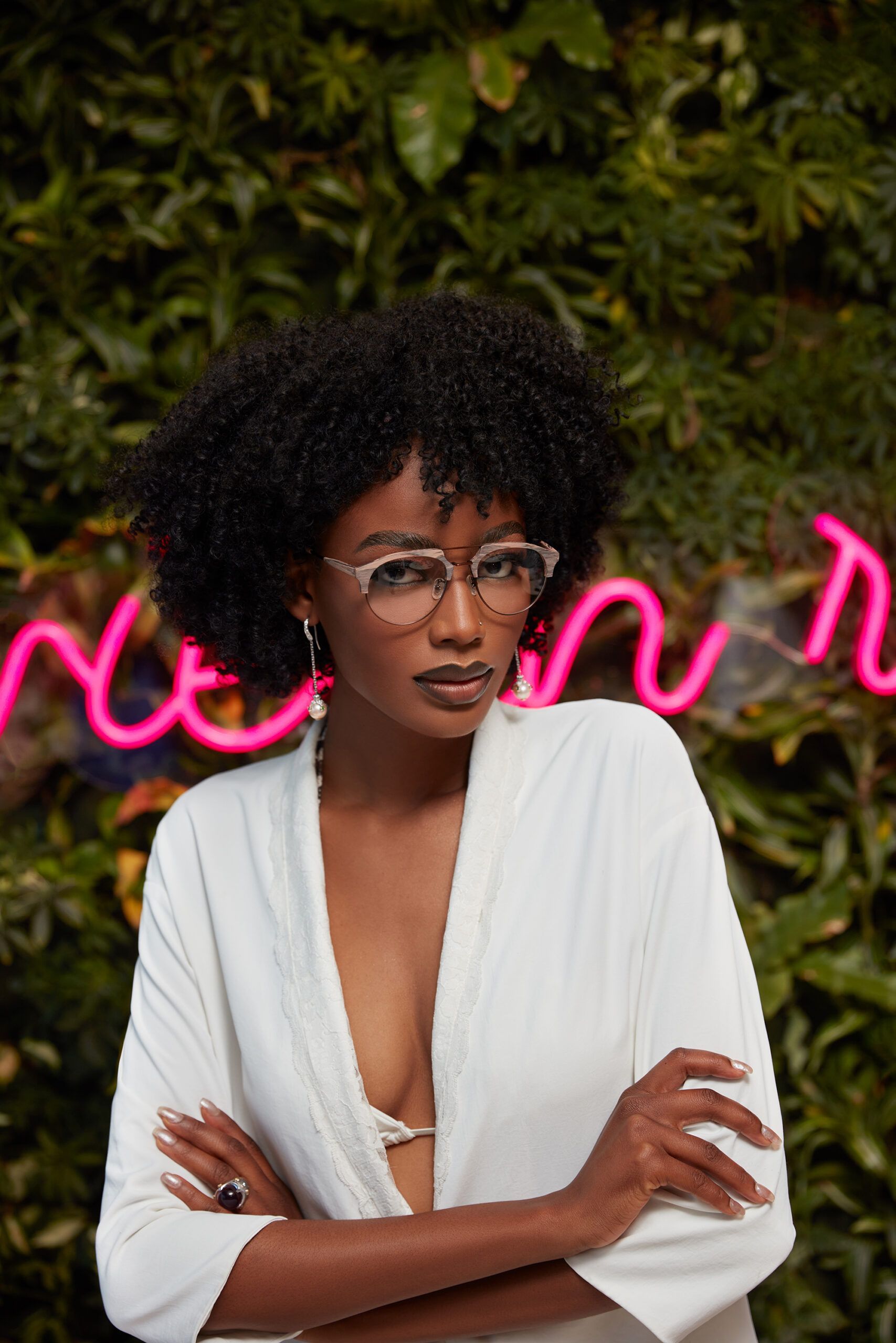 A woman wearing glasses is standing in front of a neon sign.