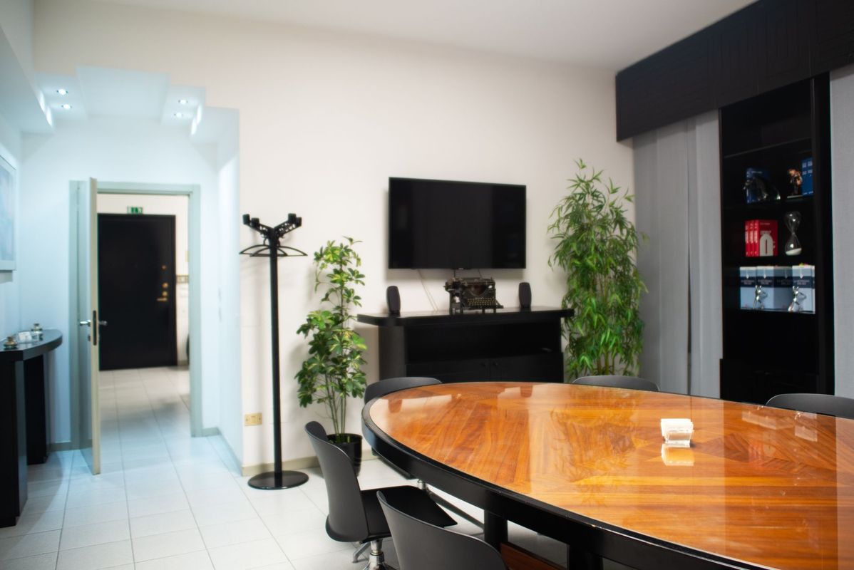 Sala da pranzo moderna con tavolo in legno lucido, TV, piante e porta con vetri colorati di blu.