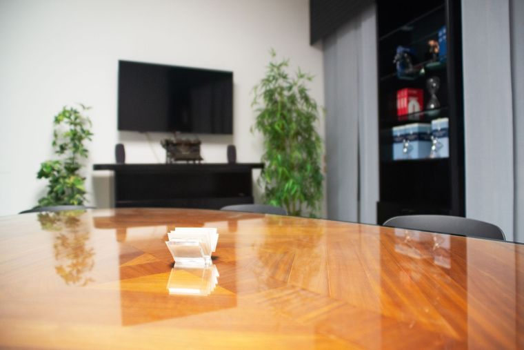 Sala riunioni moderna con tavolo in legno lucido, TV a parete e piante in vaso alte.