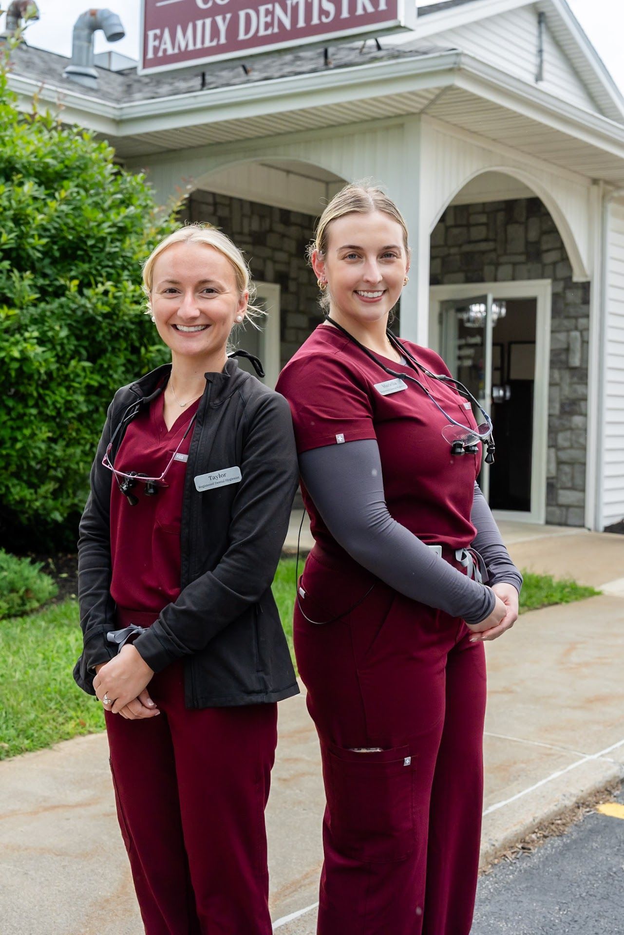 Two dental hygienists in burgundy scrubs outside Cocozzo Family Dentistry in Malta, NY