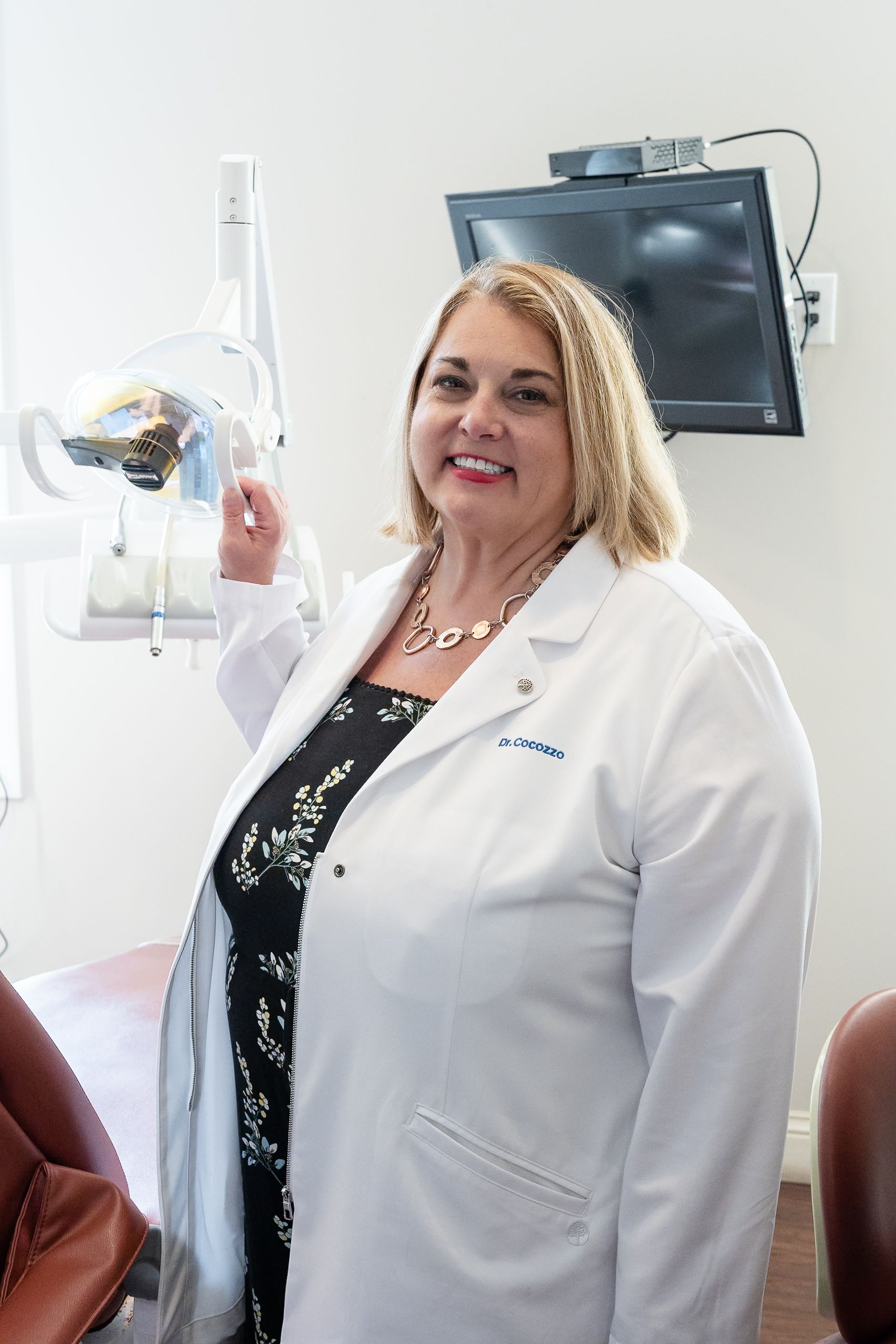 Dr. Christina Cocozzo smiling in her white coat in a treatment room at Cocozzo Family Dentistry in Malta, NY