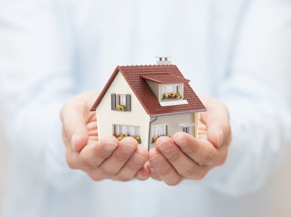 A Person is Holding a Small Model House in Their Hands — Key2 Conveyancing In Hallidays Point, NSW