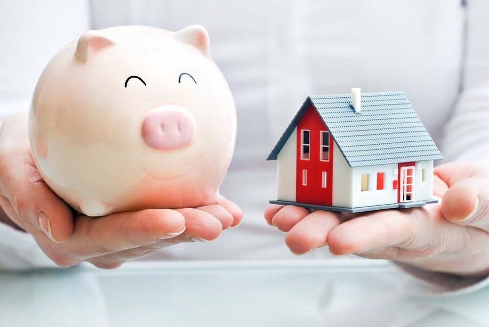 A Person is Holding a Piggy Bank and a Model House in Their Hands — Key2 Conveyancing In Tea Gardens, NSW