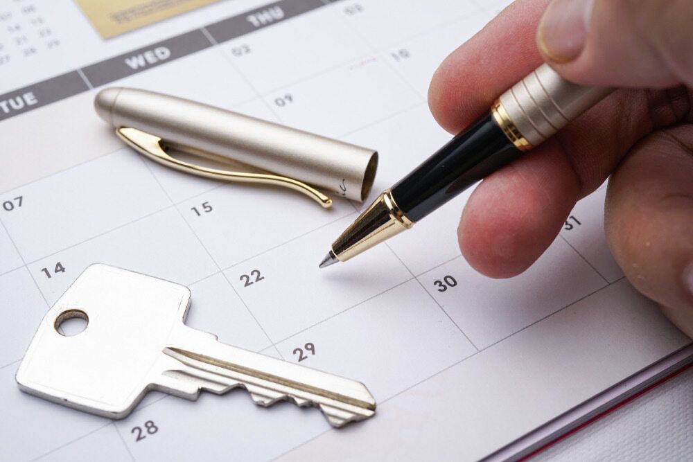 A Person is Holding a Pen Over a Calendar Next to a Key — Key2 Conveyancing In Forster, NSW